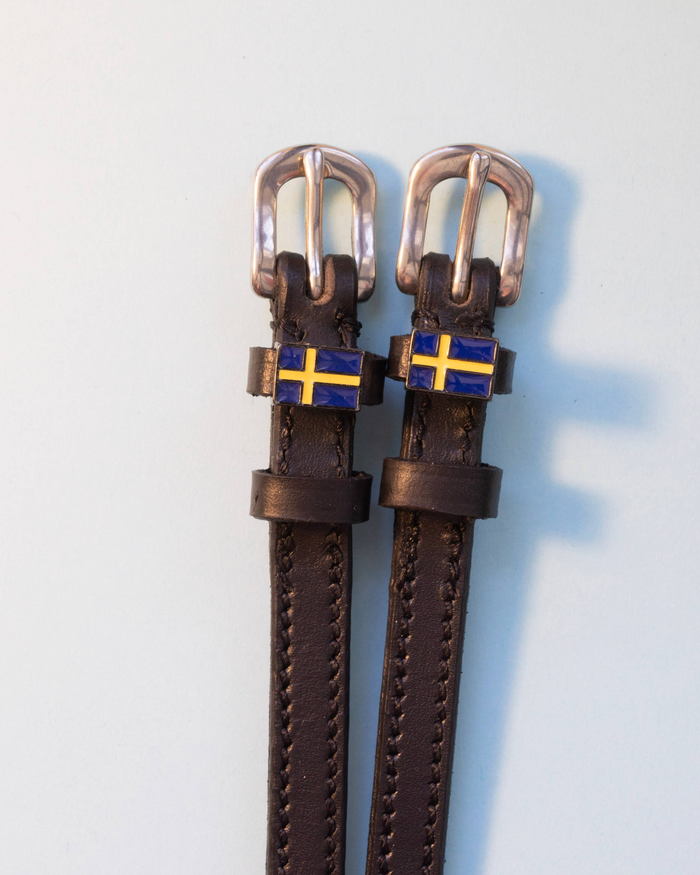 Pair of brown leather ManeJane spur straps with Swedish flag charms on grey