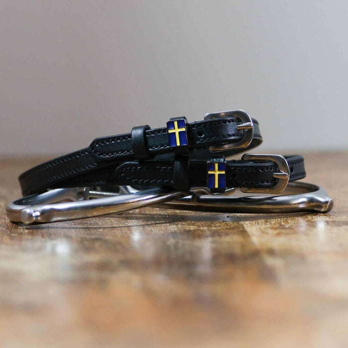 Black leather Swedish flag spur straps coiled beside a spur on wood