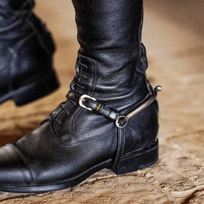 ManeJane Swedish flag spur strap fastened on a rider's black riding boot