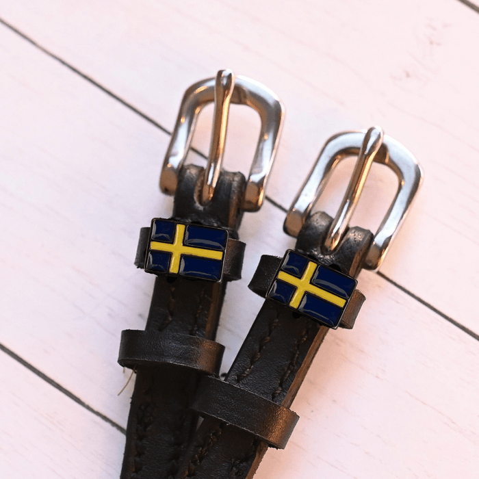 Two Swedish flag charms on dark leather spur straps over pink planks
