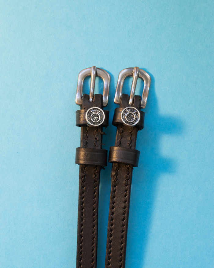 Black leather ManeJane spur straps with round Taurus zodiac charms on light blue