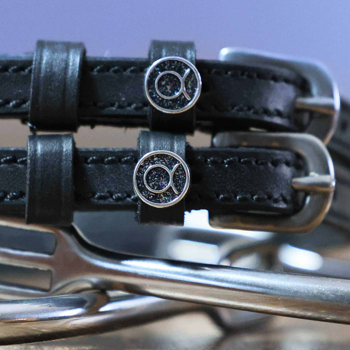 Close-up of glittery Taurus zodiac charms on black leather spur strap keepers