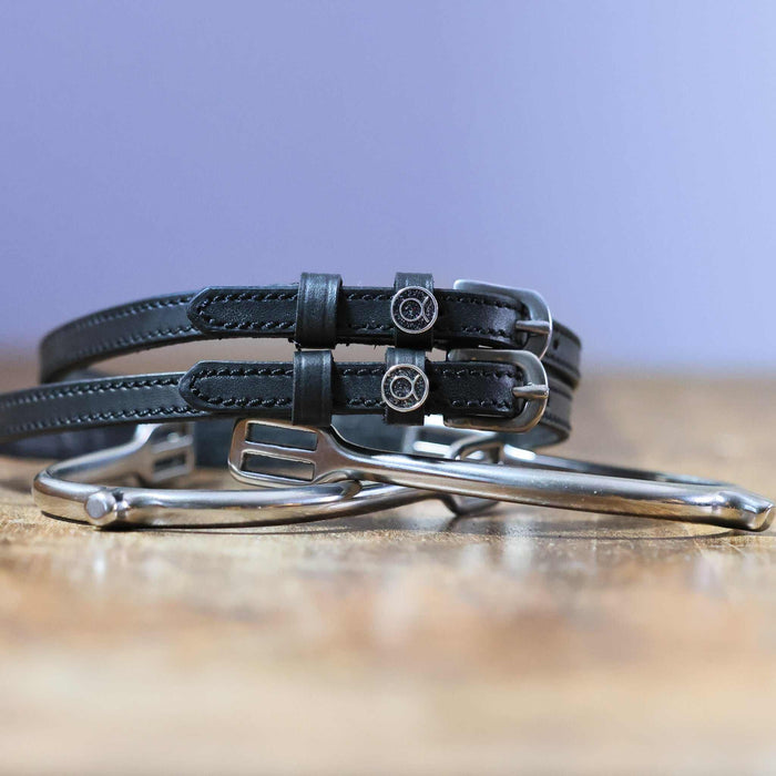 Black Taurus zodiac spur straps stacked on a silver spur on a wooden surface