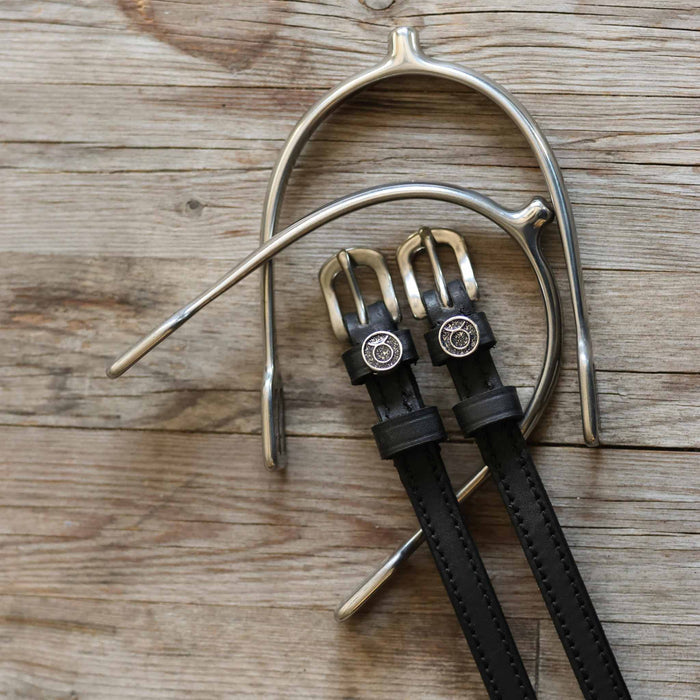 ManeJane Taurus zodiac spur straps with brass buckles beside a silver spur on wood
