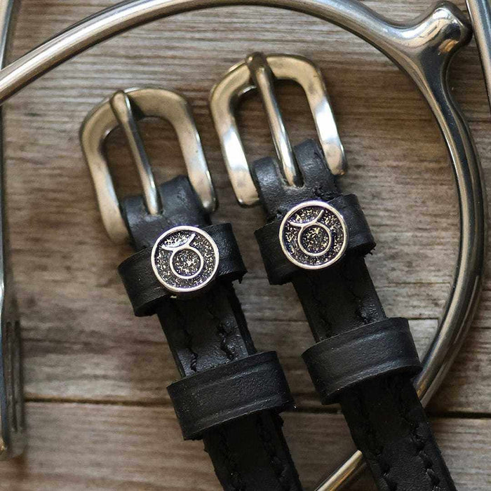 Close-up of Taurus zodiac charms and brass buckles on black leather spur straps