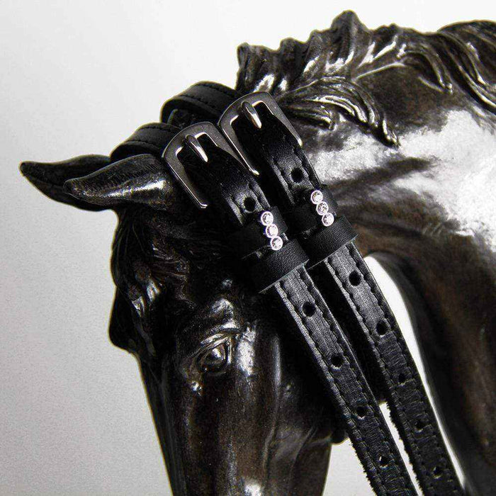 Black crystal-charm spur straps draped over a bronze horse-head sculpture
