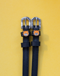 Black leather ManeJane spur straps with silver buckles and orange tiger-face charms on yellow
