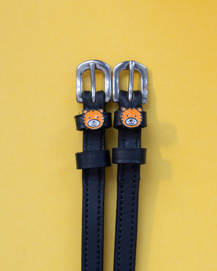Black leather ManeJane spur straps with silver buckles and orange tiger-face charms on yellow