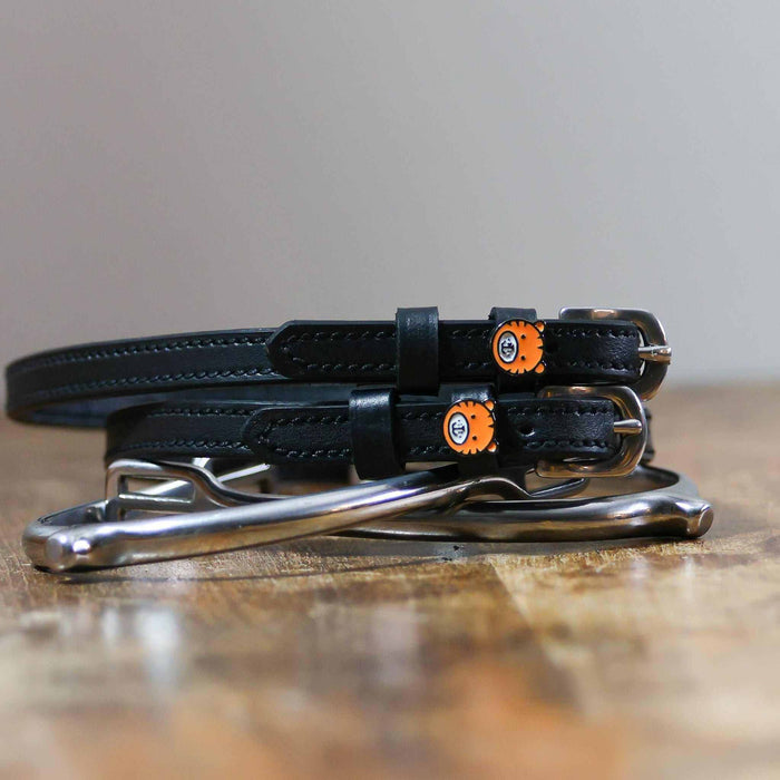 Black tiger spur straps coiled on a silver stirrup on a wooden table