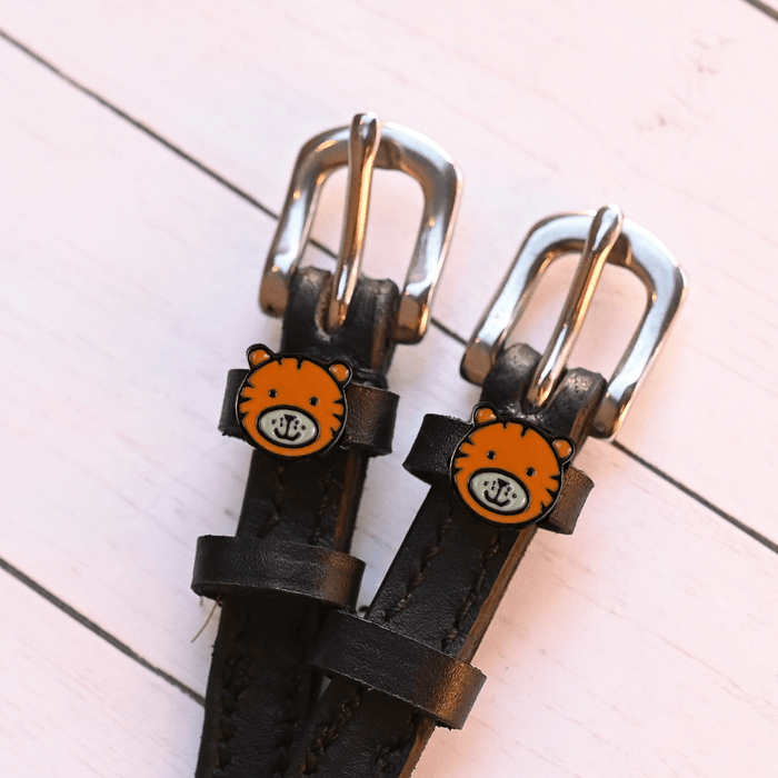 Tiger-face charm spur straps with silver buckles on pink-painted wood planks