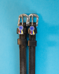 Black leather ManeJane spur straps with blue prize rosette charms on a light blue background