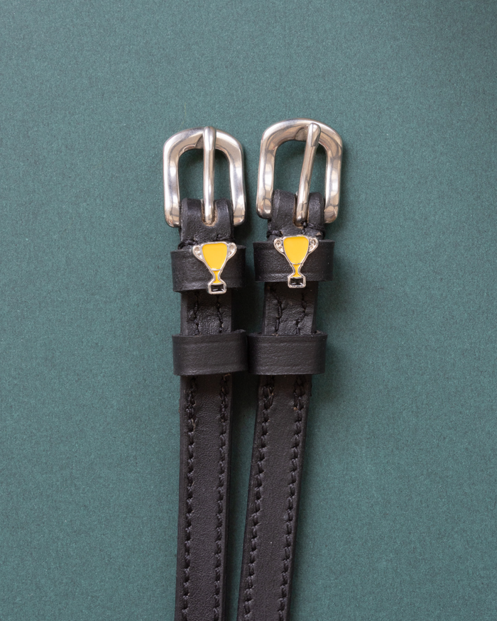 Trophy ManeJane spur straps with the signature Trophy charm, shown on a green background, by Dreamers & Schemers