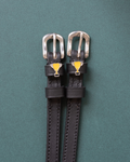 Trophy ManeJane spur straps with the signature Trophy charm, shown on a green background, by Dreamers & Schemers