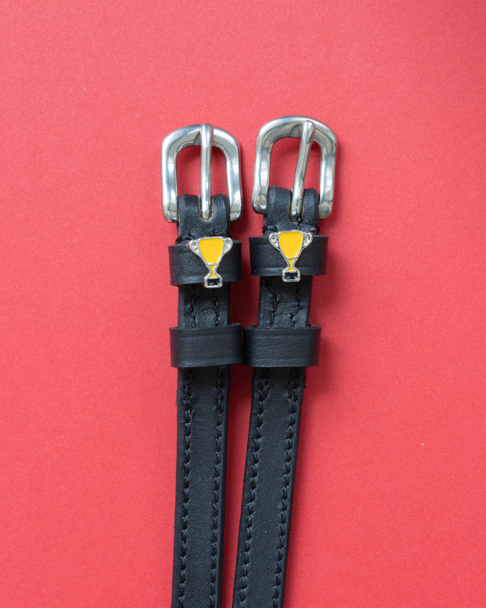 Trophy ManeJane spur straps with the signature Trophy charm, shown on a coral background