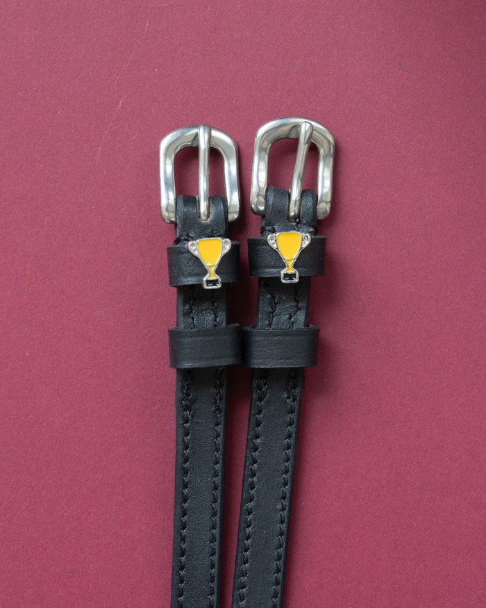 Trophy ManeJane spur straps with the signature Trophy charm, shown on a red background