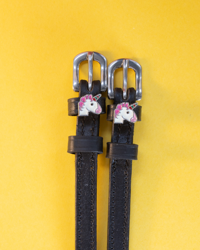 Black leather ManeJane unicorn spur straps with silver buckles, flat-laid on a yellow background