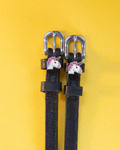 Black leather ManeJane unicorn spur straps with silver buckles, flat-laid on a yellow background