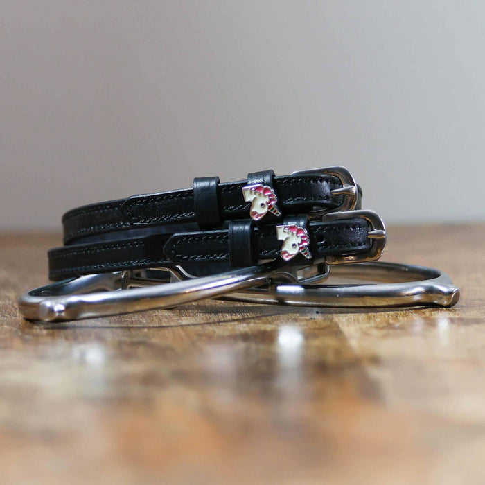 ManeJane unicorn spur straps coiled beside a silver stirrup on a wooden tabletop