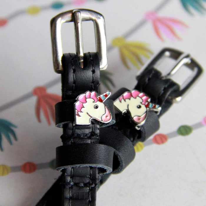 Angled view of unicorn charm ManeJane spur straps on a colorful party-streamer backdrop