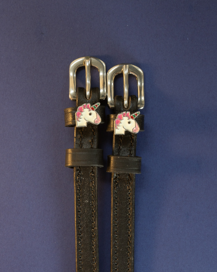 Pair of black leather unicorn spur straps laid flat on a deep navy background