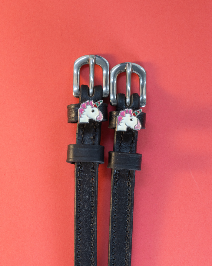 Black leather ManeJane unicorn spur straps with silver buckles on a red background
