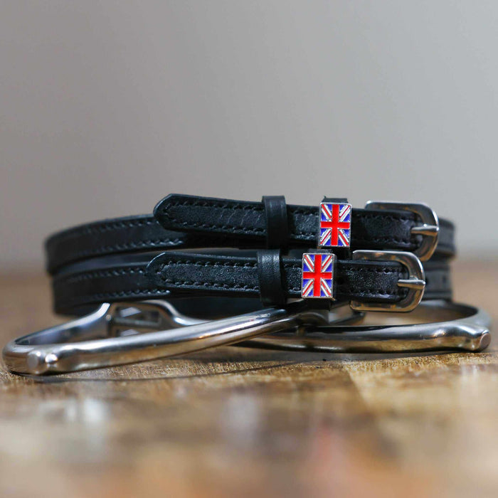 Coiled black leather Union Jack flag spur straps stacked on a silver spur on wood
