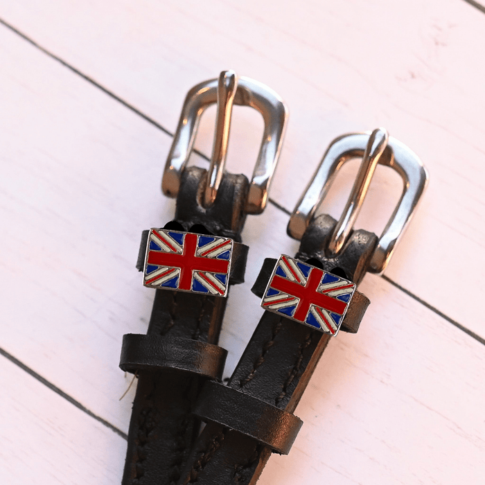 Overhead of black leather spur straps with silver buckles and Union Jack charms on pink wood