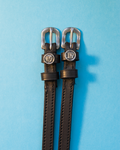 Black leather ManeJane spur straps with round Virgo zodiac charms on a light blue background