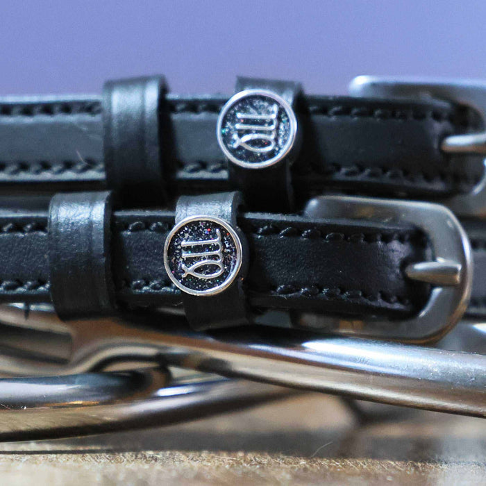 Close-up of round Virgo zodiac charms on black leather ManeJane spur strap keepers