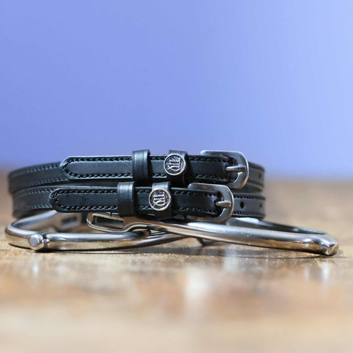 Black leather Virgo zodiac spur straps coiled beside a silver spur on wood