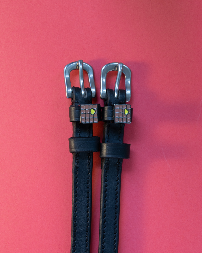 Black leather ManeJane spur straps with waffle-and-butter charms on red