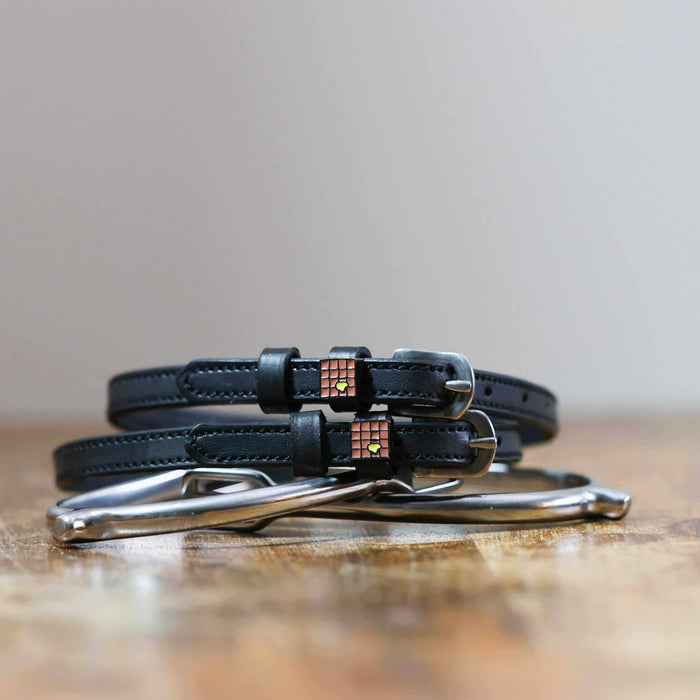 Black leather waffle spur straps coiled on wood beside a stirrup