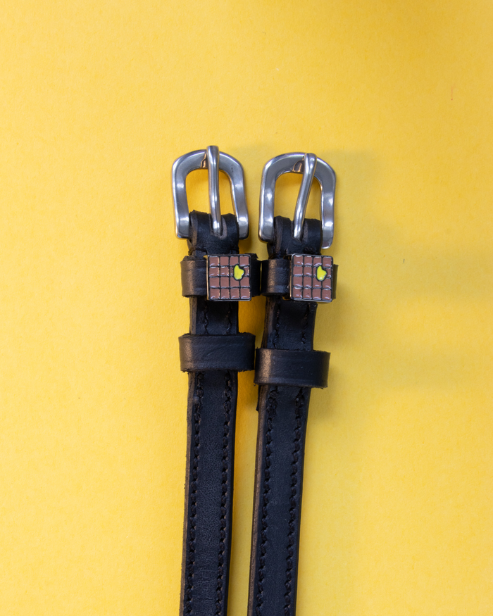 Pair of waffle-charm spur straps laid flat on a yellow background