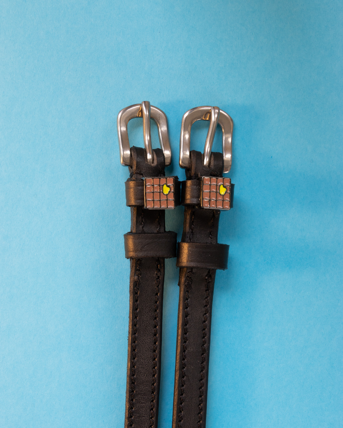 Black leather waffle spur straps laid flat on a light blue background
