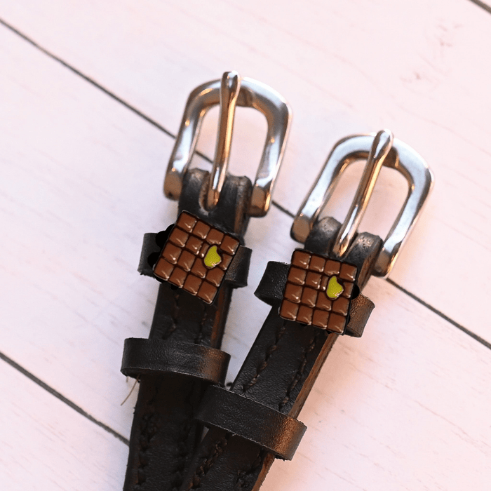 Angled close-up of waffle-and-butter spur strap charms on pale pink planks