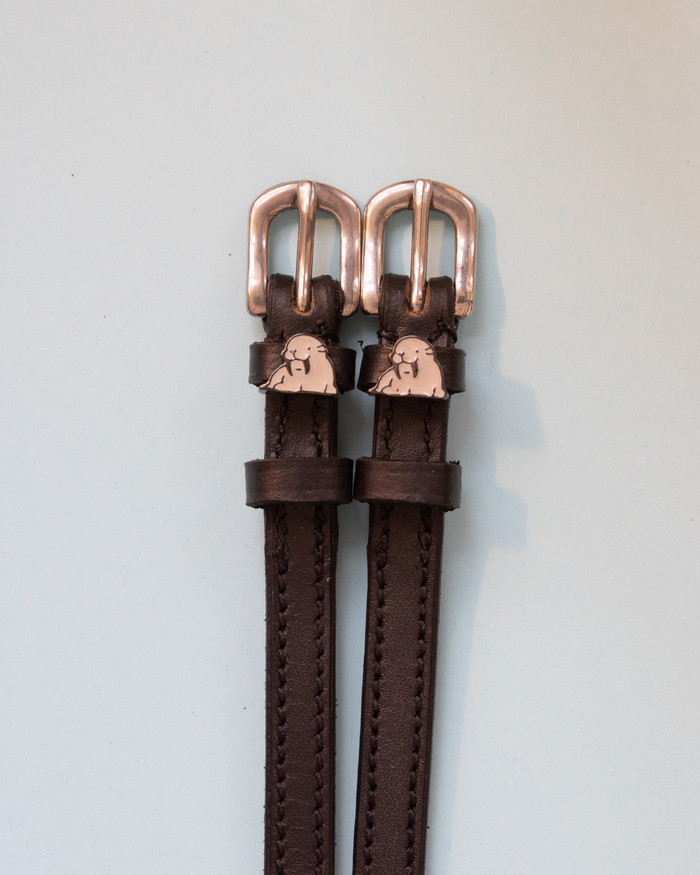Close-up of grey walrus charms with tusks on black leather ManeJane spur strap keepers