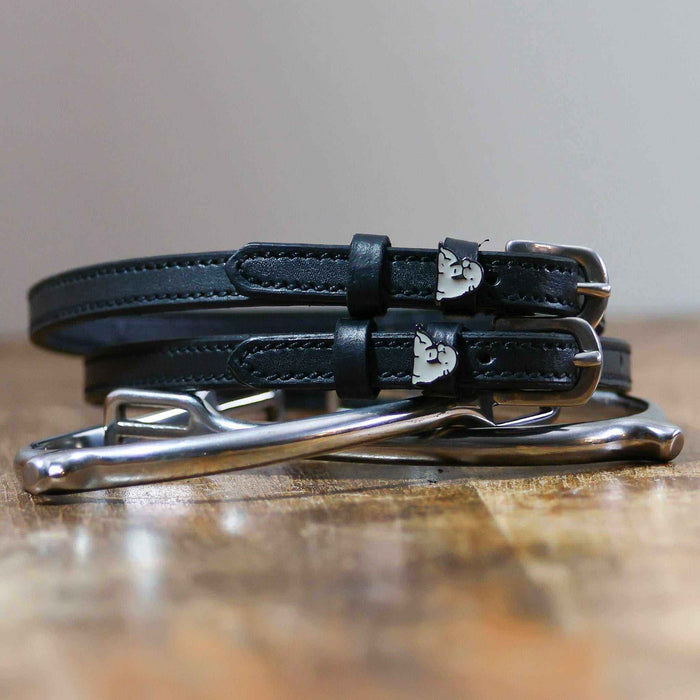 Black leather walrus spur straps with silver buckles angled on white wooden planks