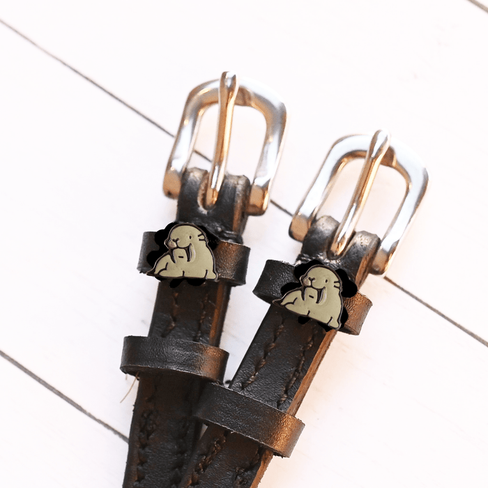 Grey walrus charm spur straps with silver buckles displayed on white wood planks