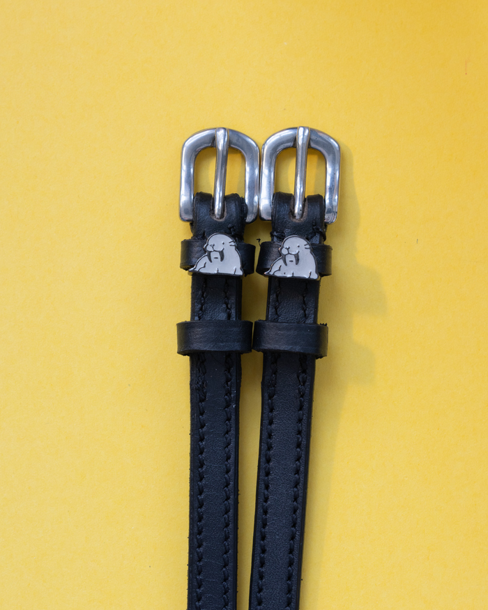 Black leather walrus spur straps with silver buckles on a yellow background