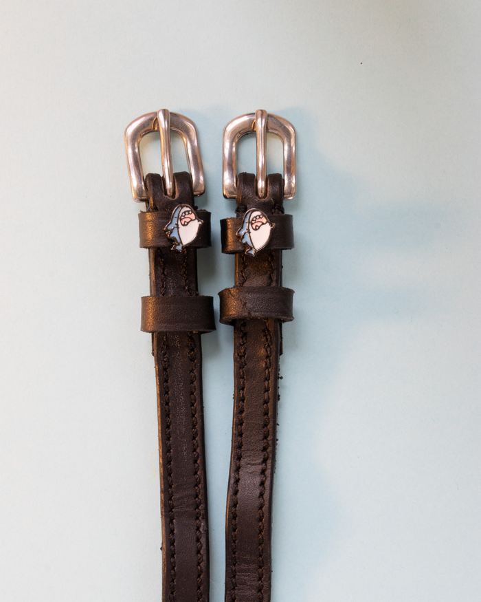 Black leather ManeJane spur straps with silver buckles and blue shark head charms on grey-blue