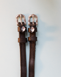 Black leather ManeJane spur straps with silver buckles and blue shark head charms on grey-blue