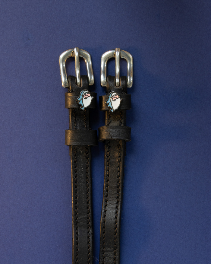 Wild Shark spur straps in black leather with silver buckles laid flat on a navy background