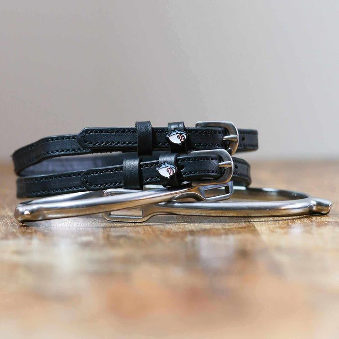 Black leather Wild Shark spur straps coiled beside a silver spur on a wood surface