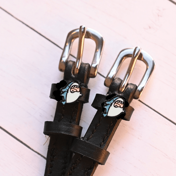 Silver buckles and shark head charms of black leather spur straps on pink painted wood